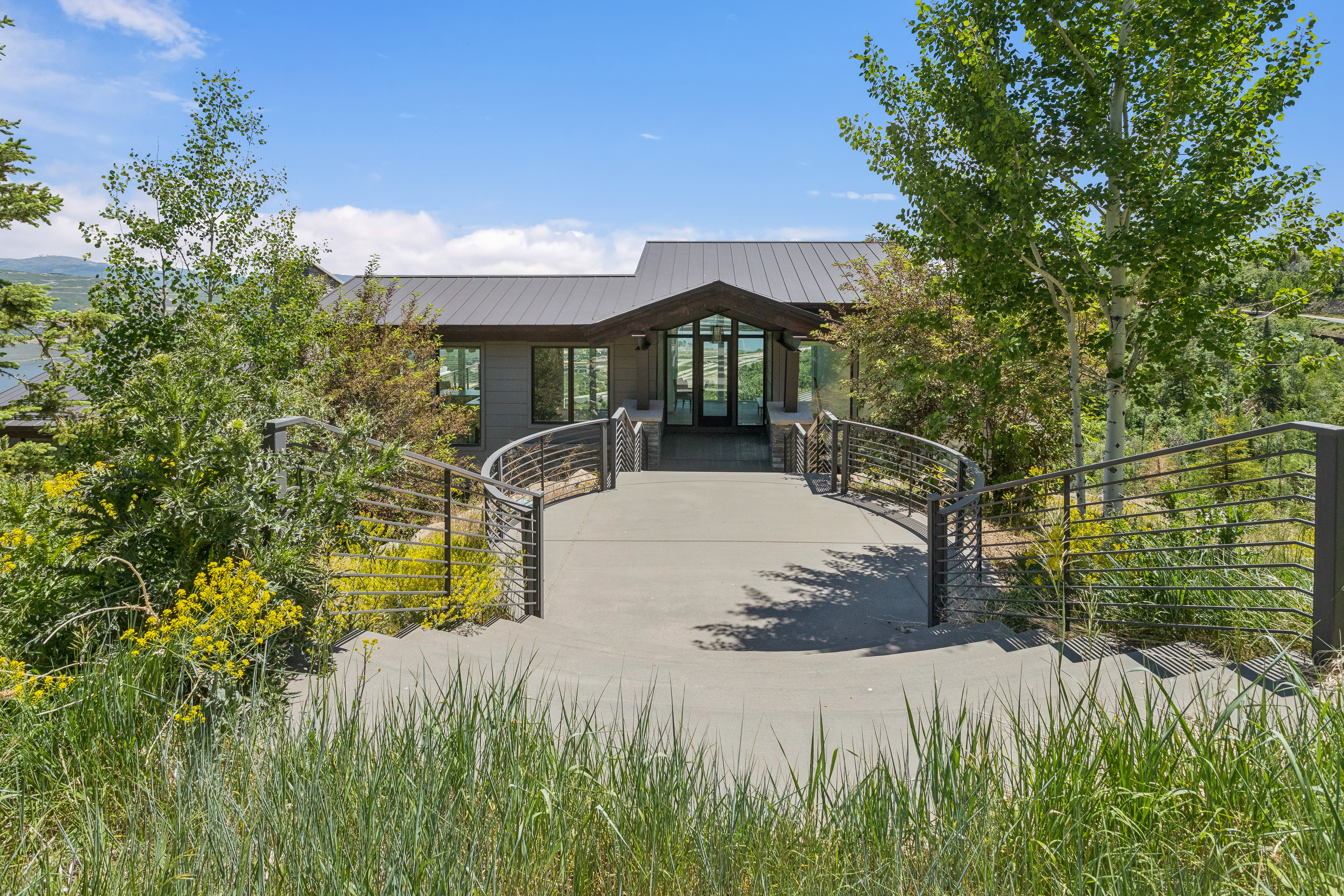 Contemporary exterior featuring a metal roof, expansive windows, and a curved concrete entryway with modern cable railings