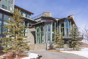 Contemporary multi-level exterior with extensive glazing, stone facade accents, multiple rooflines, a multi-tiered stone staircase, and an upper-level balcony