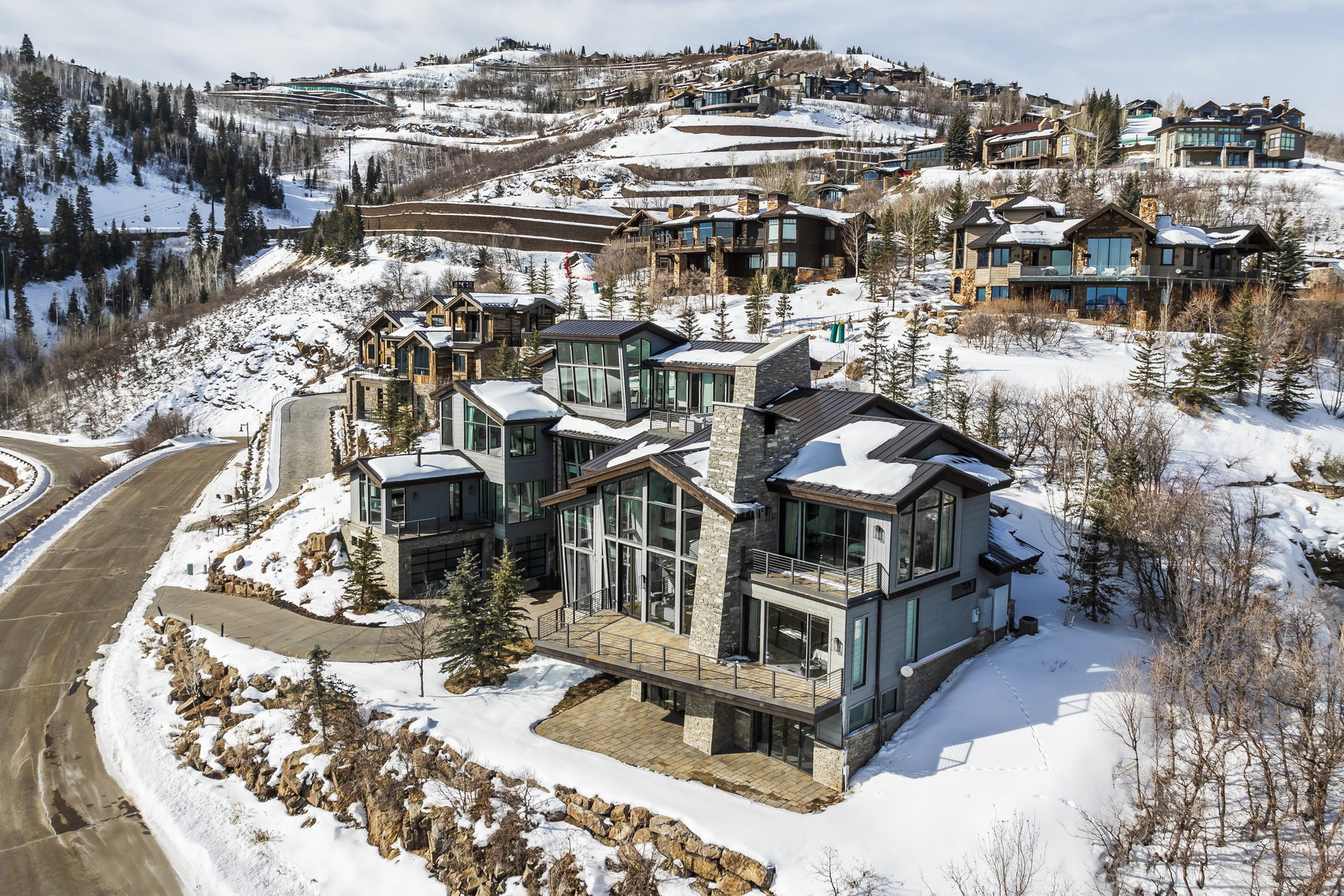 Contemporary mountain residence featuring multiple levels, extensive glazing, a stone chimney, and balconies