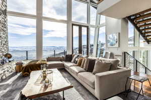 Great room featuring a floor-to-ceiling window wall, stacked stone fireplace, exposed wood staircase, and wood-finish flooring