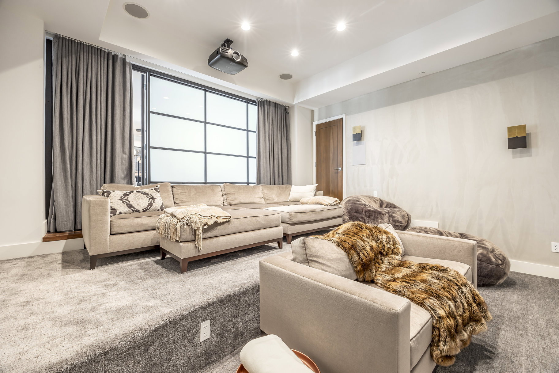 Media room with tiered carpeted flooring, a large multi-pane window, and a ceiling-mounted projector