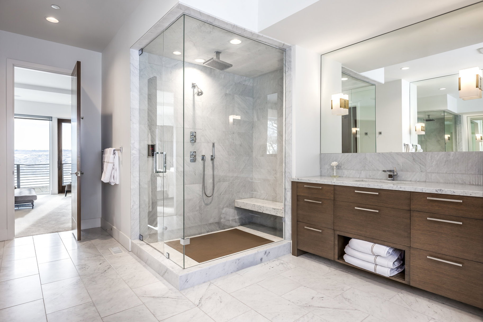Contemporary bathroom featuring a spacious glass-enclosed shower with a bench, dual shower heads, and marble-style tiling