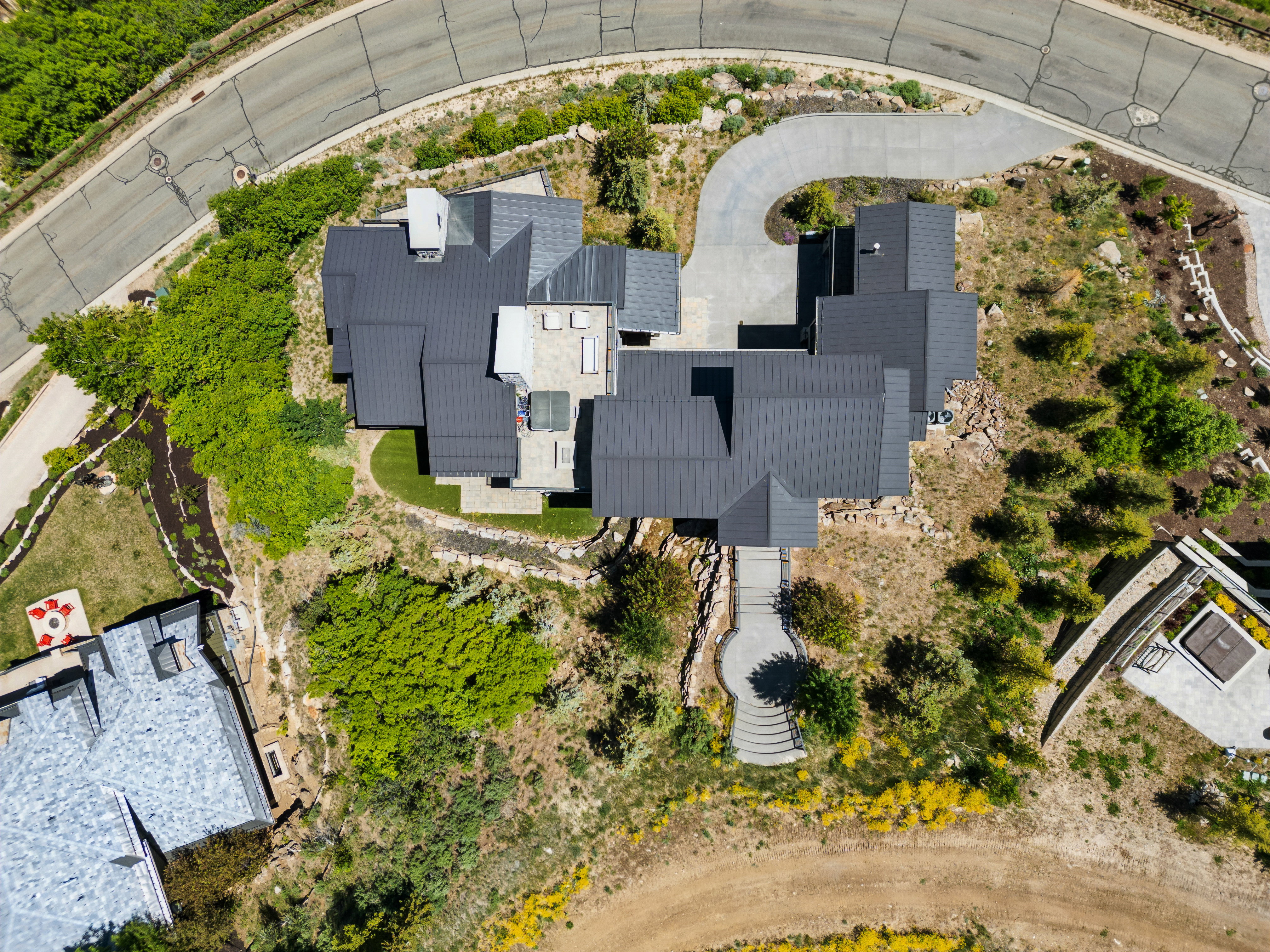 Architectural residence featuring a multi-level dark metal roof and a winding concrete driveway