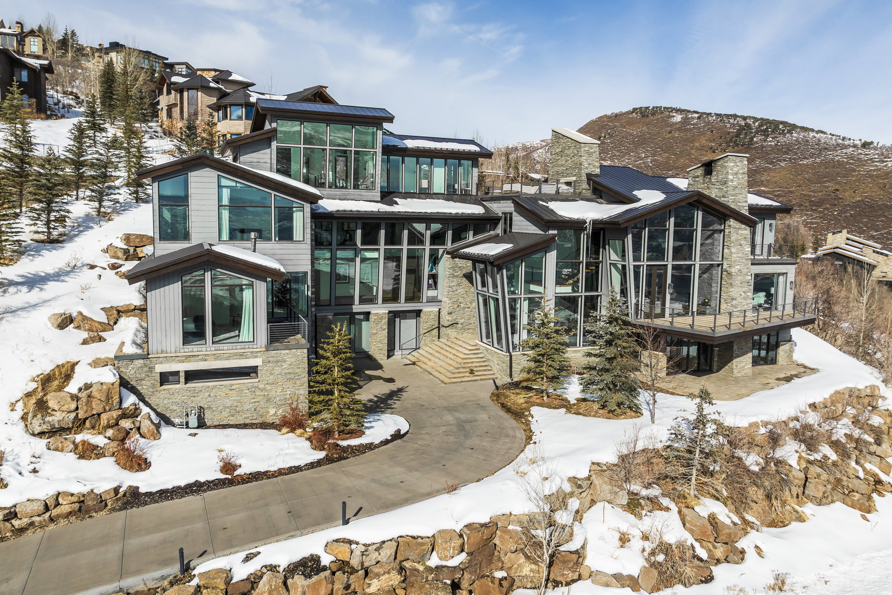 Contemporary multi-level residence featuring expansive window walls, stone accents, multiple balconies, and a paved circular driveway