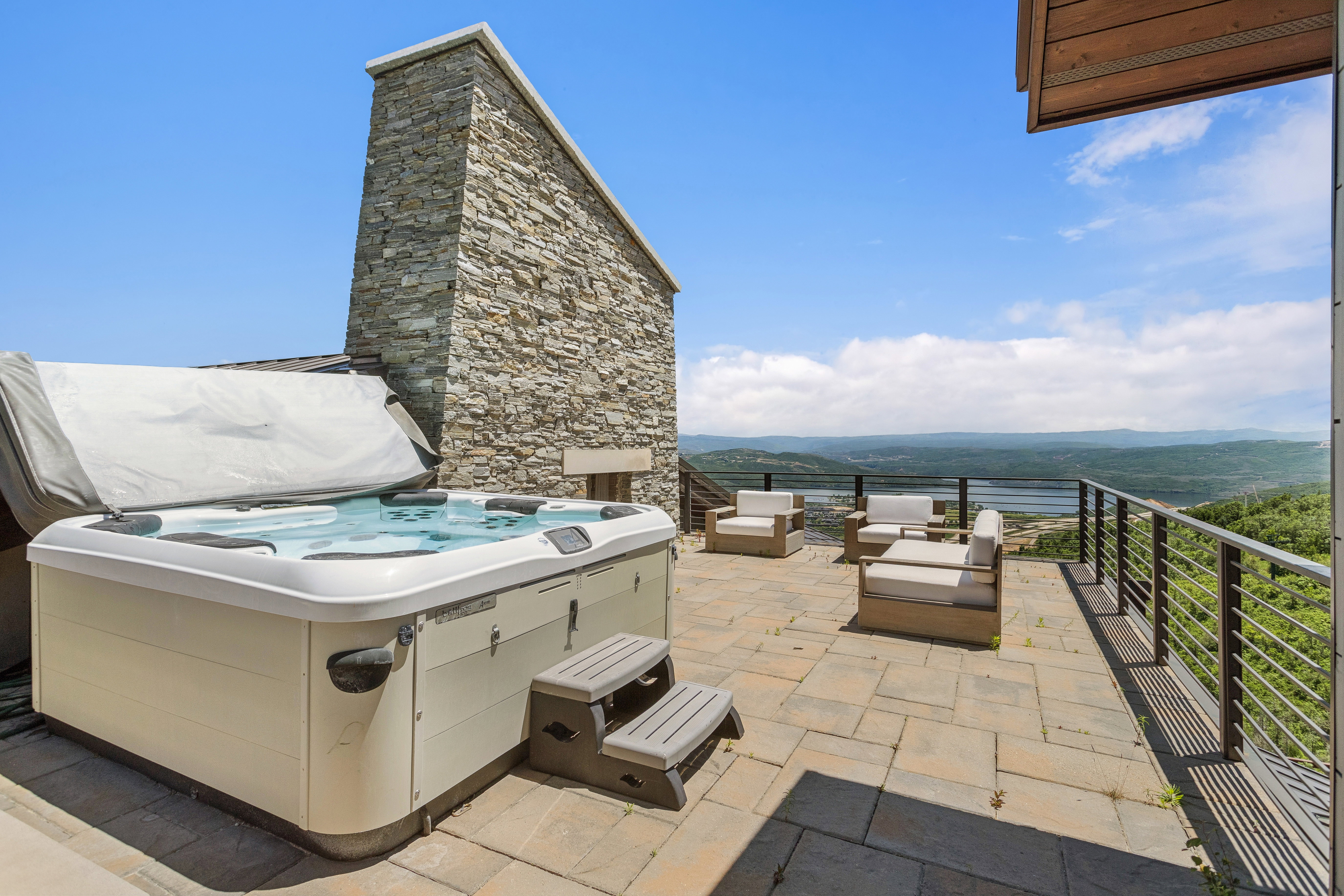 Expansive stone patio featuring a built-in hot tub, a natural stone chimney, and a cable railing system