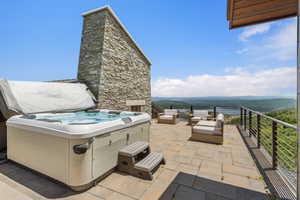 Expansive stone patio featuring a built-in hot tub, a natural stone chimney, and a cable railing system