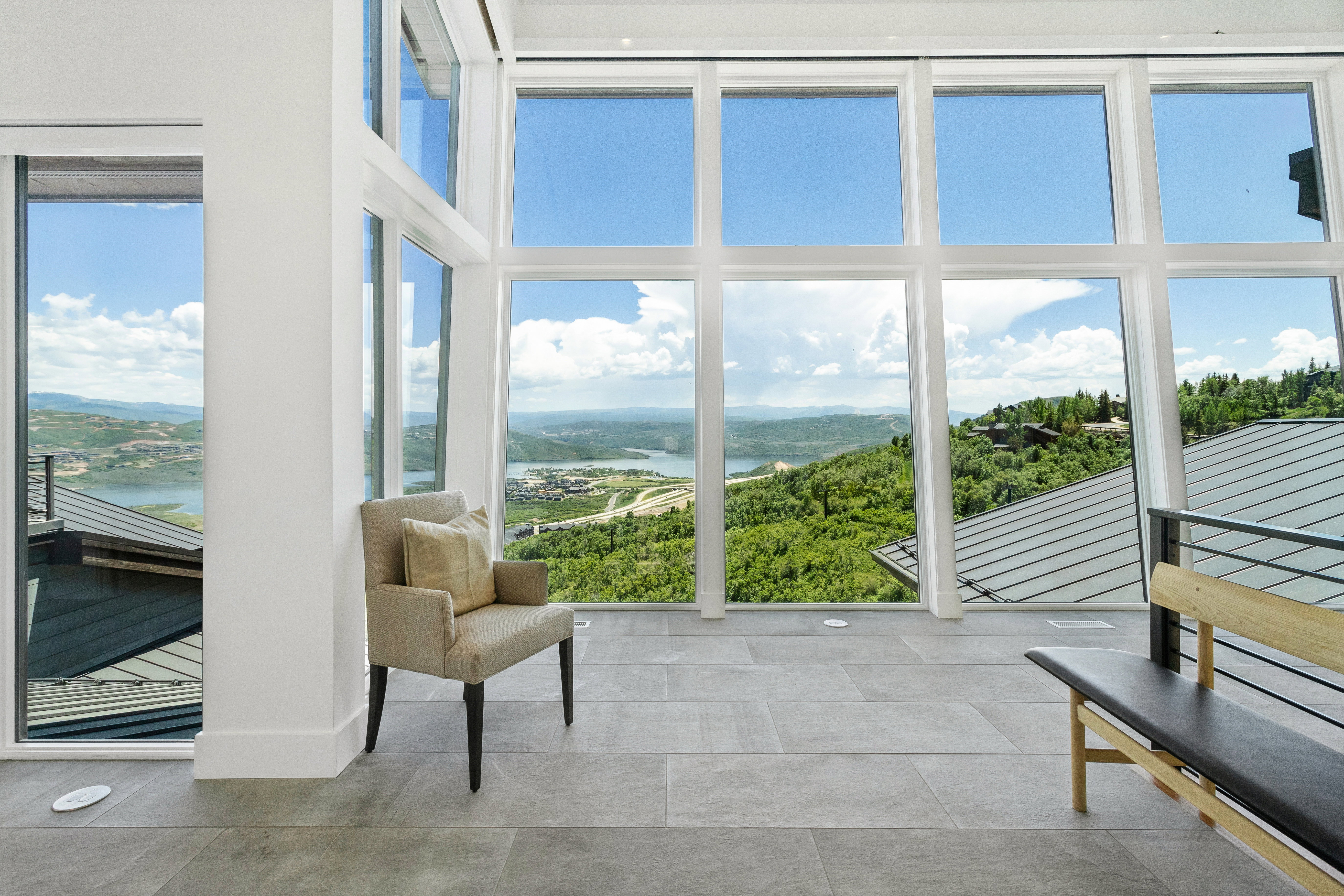 Expansive floor-to-ceiling windows with white frames, showcasing distant water and lush green hills