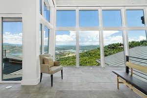 Expansive floor-to-ceiling windows with white frames, showcasing distant water and lush green hills
