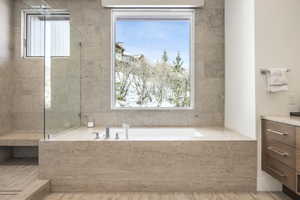 Integrated soaking tub with chrome fixtures, surrounded by stone tile walls and flooring