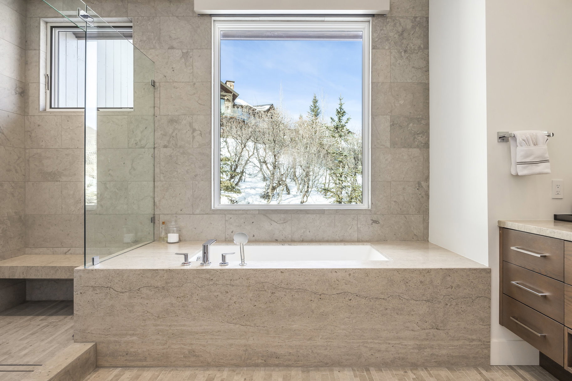 Built-in soaking tub with deck-mounted fixtures, surrounded by large format stone tile