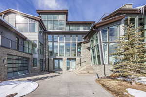 Contemporary architectural exterior featuring extensive window walls, stacked stone accents, horizontal siding, and a glass-paneled garage door