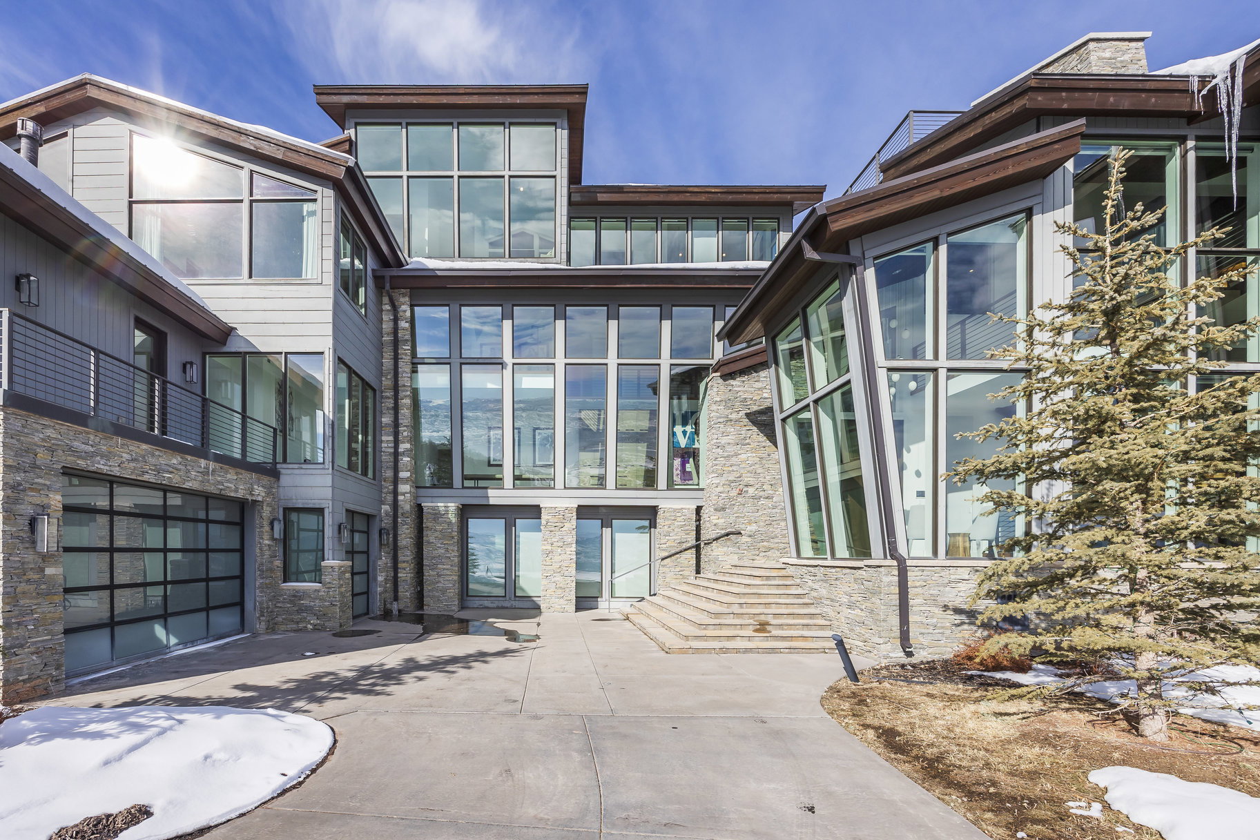 Contemporary multi-level exterior featuring extensive glazing, stone accents, horizontal siding, and a glass-paneled garage door