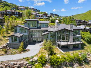 Expansive modern residence featuring multiple levels, extensive glazing, a stone chimney, a large outdoor deck, and a paved driveway
