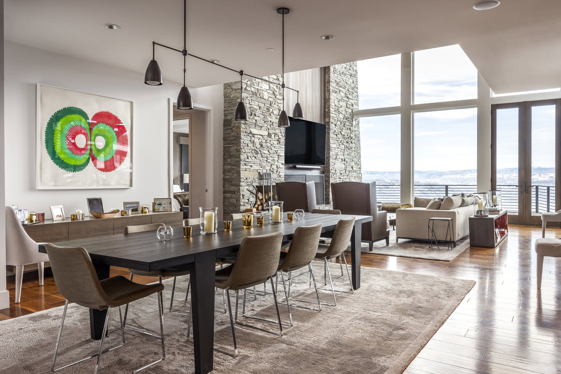 Open-concept interior featuring wood-finish flooring, a stone accent wall, and expansive windows