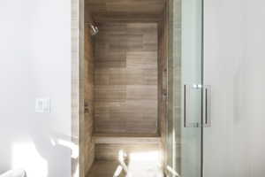 Walk-in shower featuring natural tone tile, a built-in bench, recessed shelving, a glass door, and a polished chrome showerhead