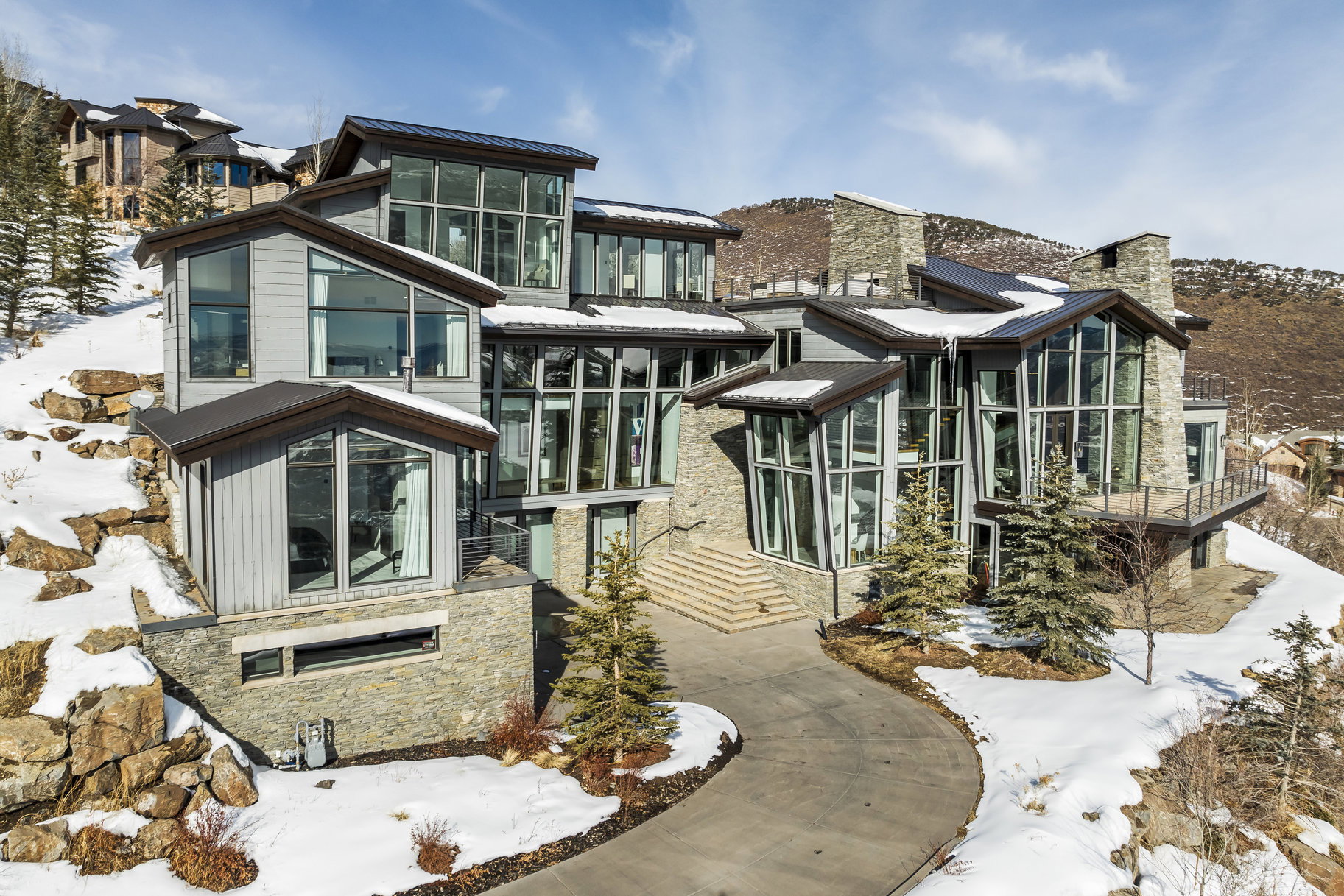 Modern architectural residence featuring multiple stone accent walls, extensive floor-to-ceiling windows, and multi-level rooflines