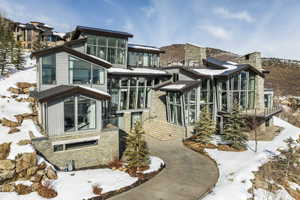Modern architectural residence featuring multiple stone accent walls, extensive floor-to-ceiling windows, and multi-level rooflines