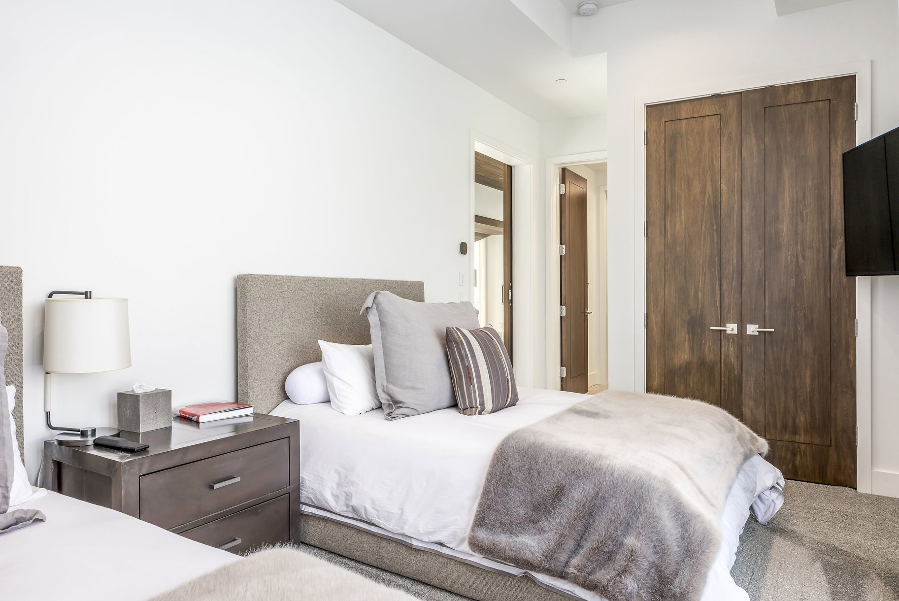Bedroom featuring twin beds with upholstered headboards, a dark wood-finish nightstand, sleek wall-mounted lighting, and double bi-fold doors with modern hardware