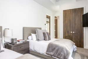 Bedroom featuring twin beds with upholstered headboards, a dark wood-finish nightstand, sleek wall-mounted lighting, and double bi-fold doors with modern hardware