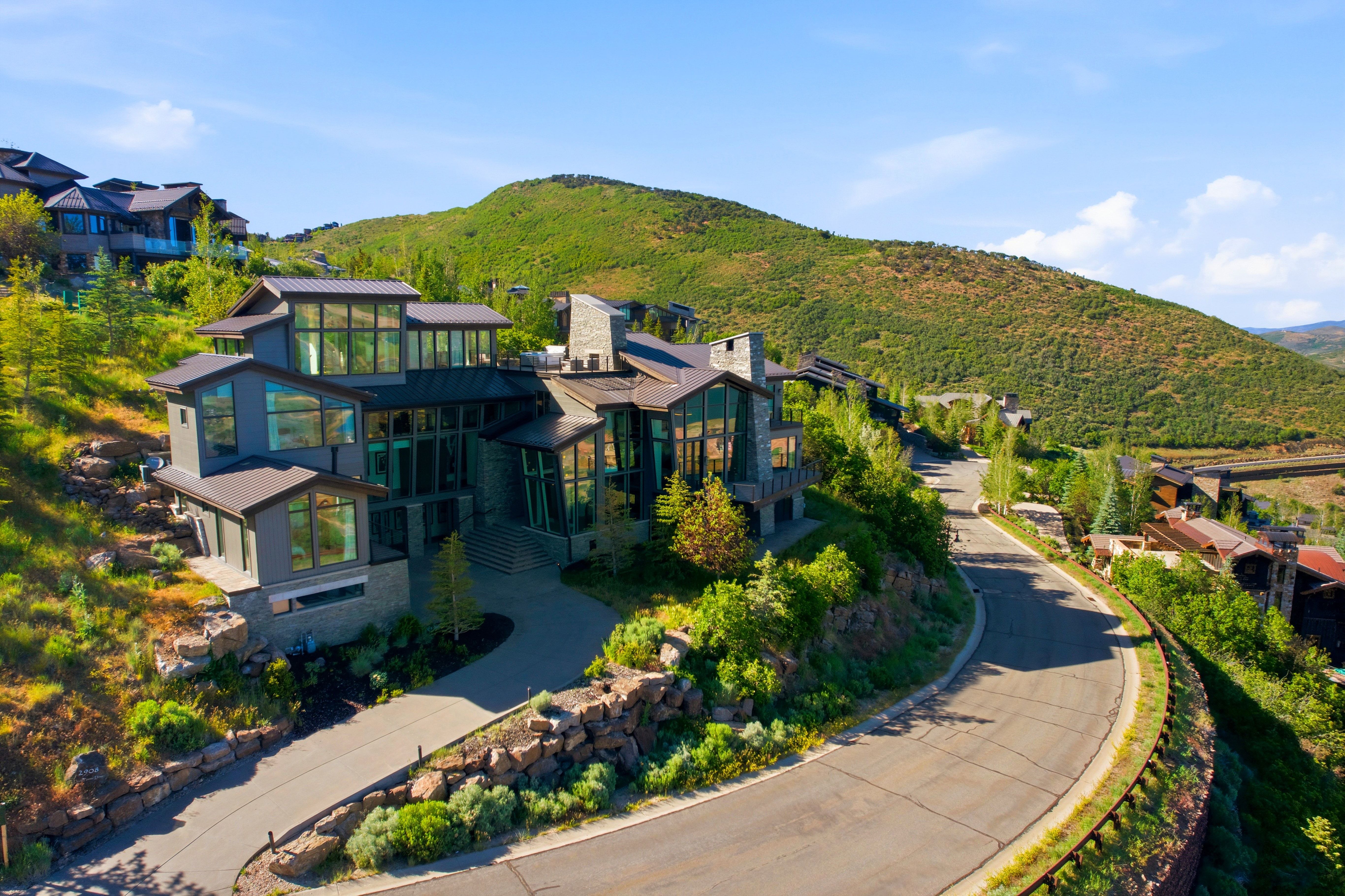 Contemporary multi-level residence featuring expansive windows, a stone and dark siding exterior, and a prominent driveway