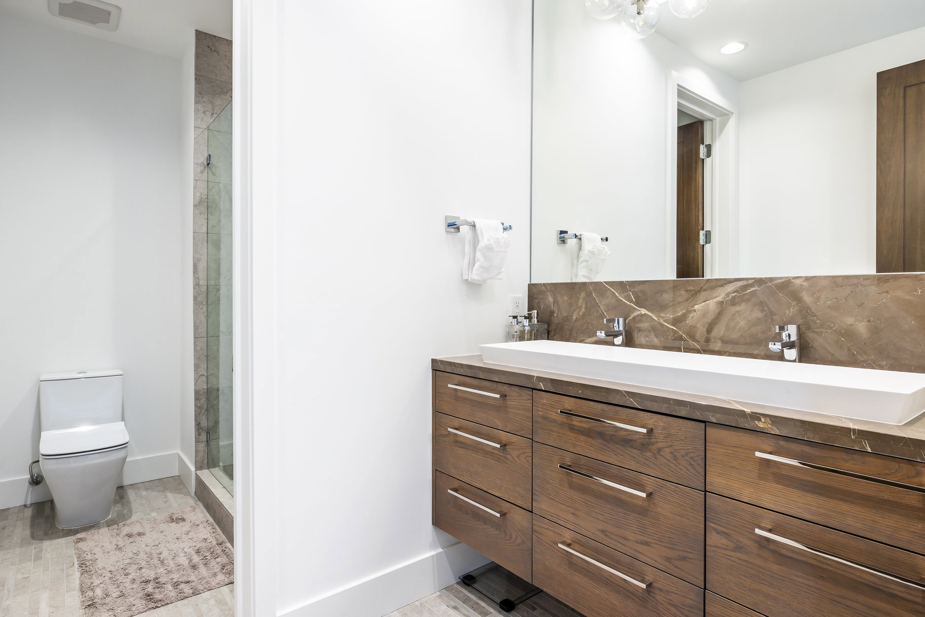 Bathroom featuring a dual-sink vanity with wood-finish cabinetry, a stone countertop, and an integrated rectangular basin