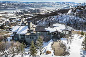 Modern architectural residence featuring a prominent stone chimney, multiple outdoor terrace spaces, extensive glazing, a distinct covered entryway, and a winding paved walkway