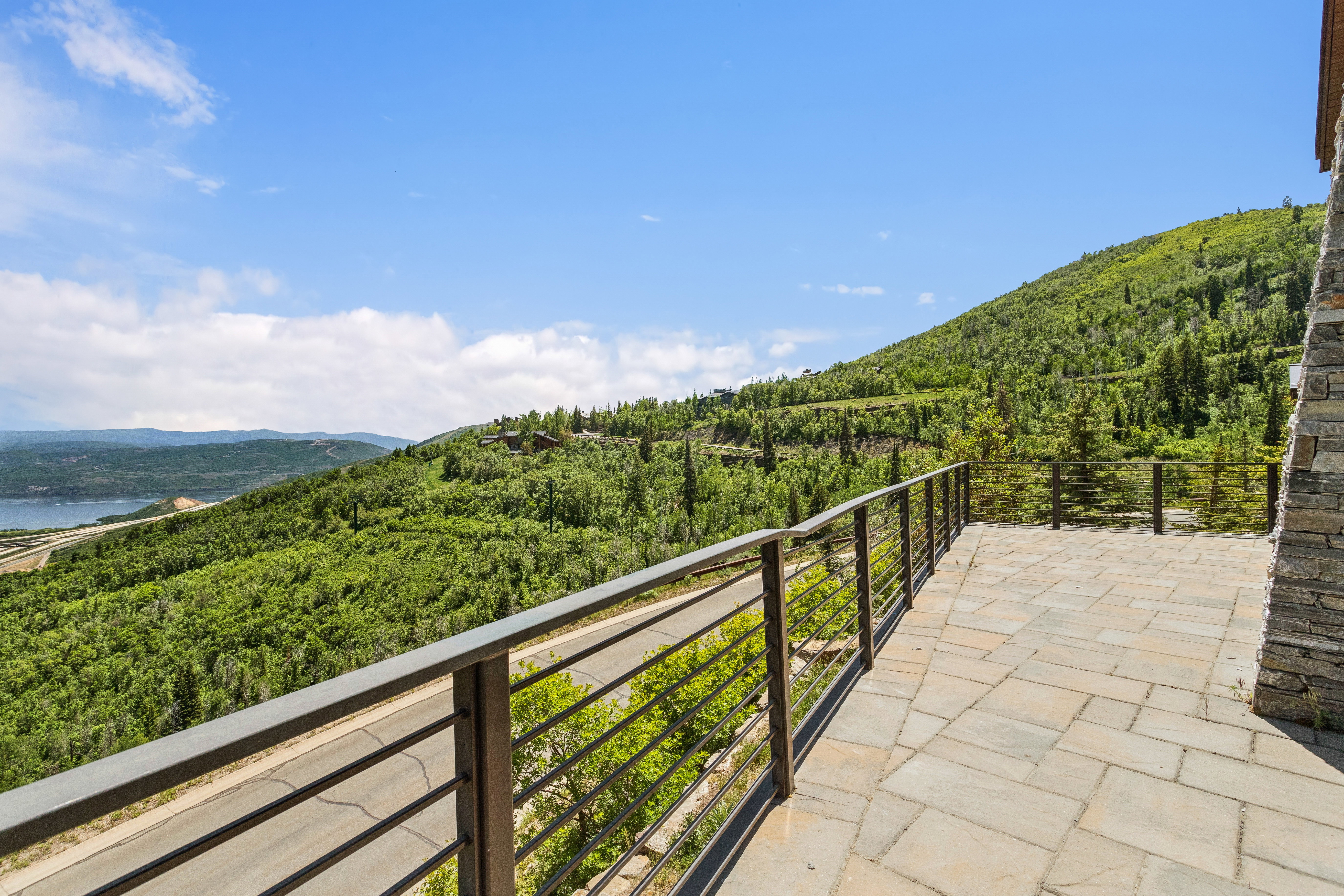Spacious stone paver patio featuring metal horizontal railings and a stacked stone exterior wall