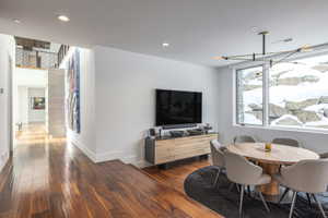 Open-concept living area featuring rich wood-finish flooring, recessed lighting, and a modern linear chandelier