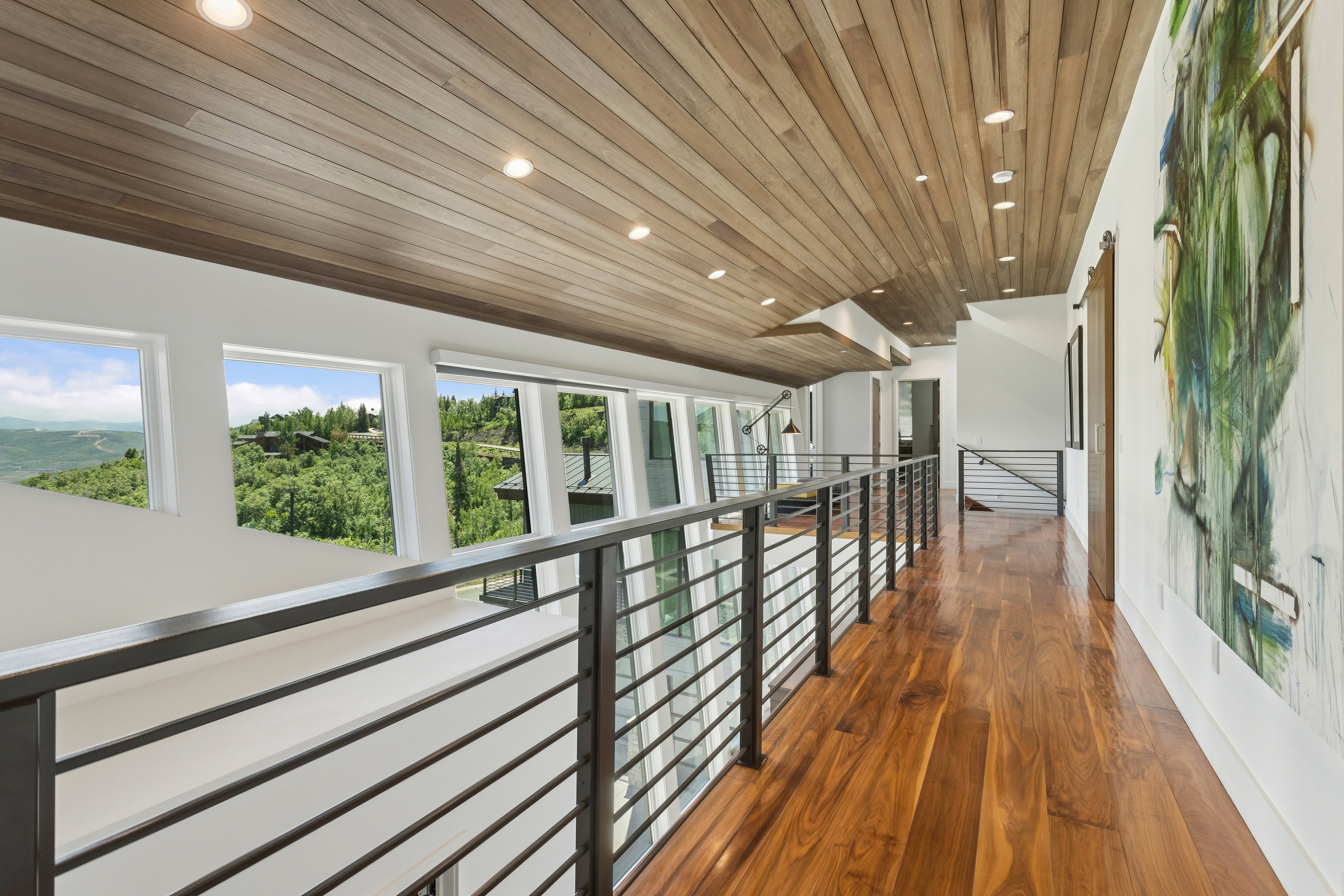 Upper-level hallway featuring wood-finish flooring, a wood-paneled ceiling with recessed lighting, and a contemporary metal railing system