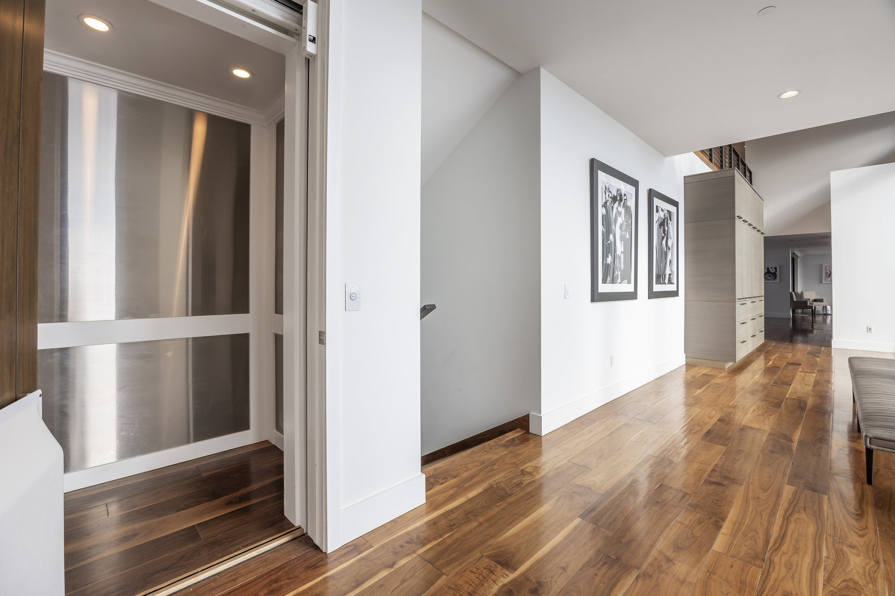 Residential elevator with brushed metal interior, recessed lighting, and wood-finish flooring
