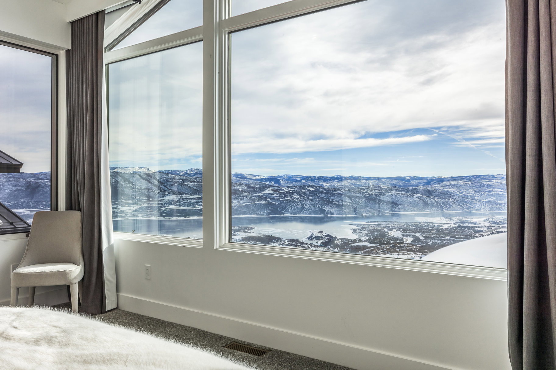 Expansive window wall with white framing showcasing a wide-ranging mountain, lake, and distant cityscape scenery