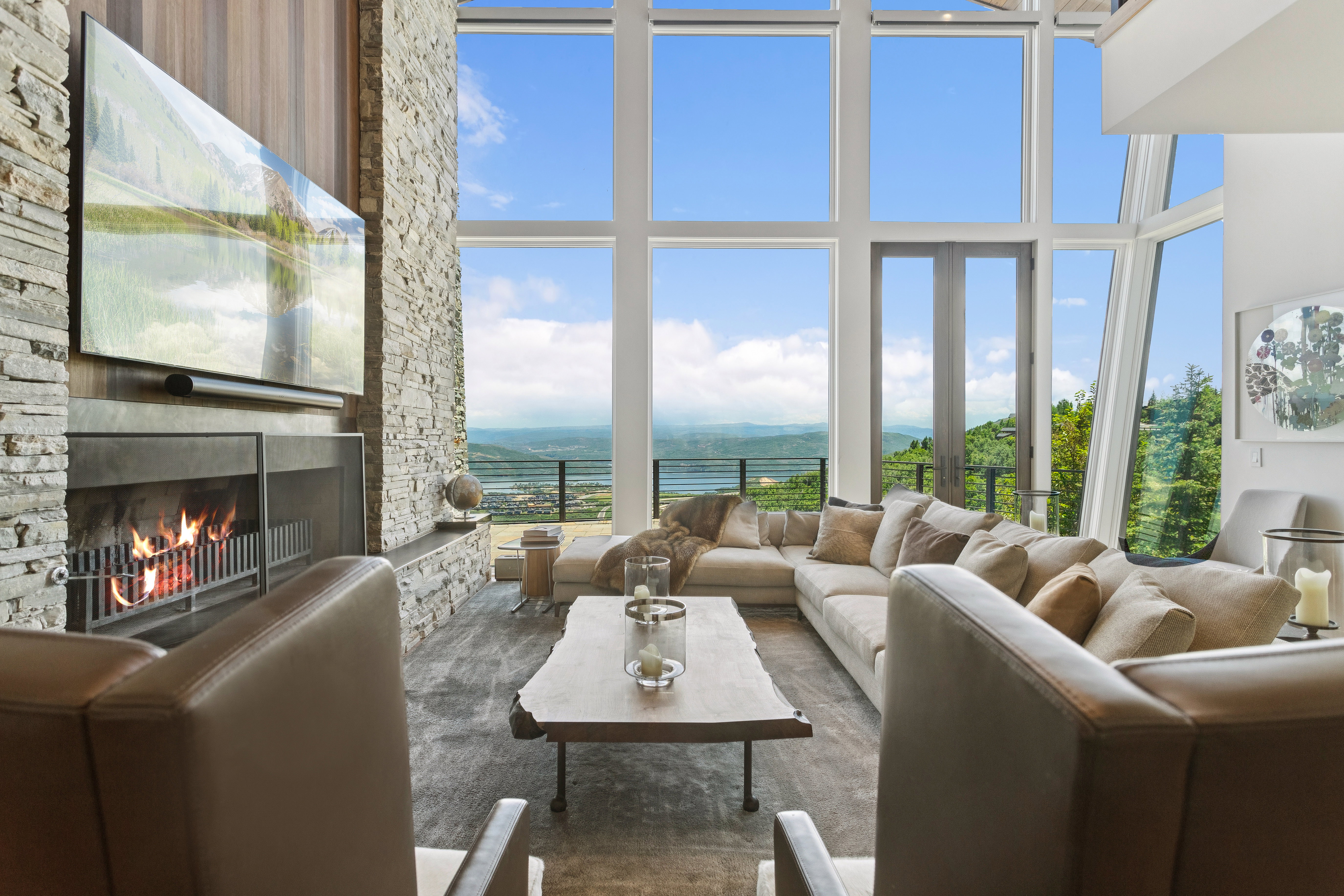 Living area featuring a floor-to-ceiling stone fireplace with a wood mantel, expansive windows, and glass doors opening to an outdoor railing