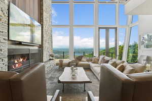Living area featuring a floor-to-ceiling stone fireplace with a wood mantel, expansive windows, and glass doors opening to an outdoor railing