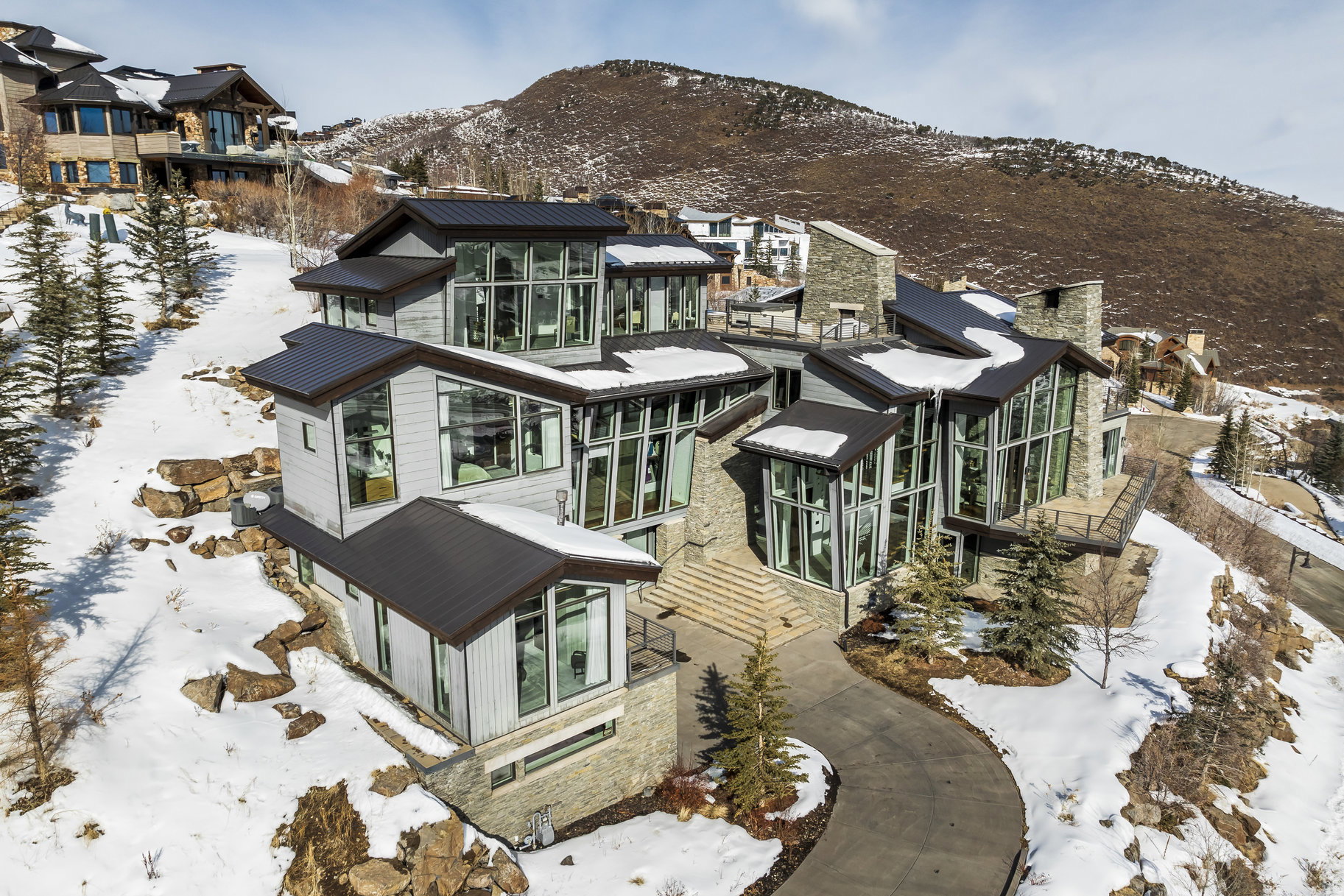 Contemporary multi-level residence featuring extensive glass facades, stone accents, and dark metal roofing