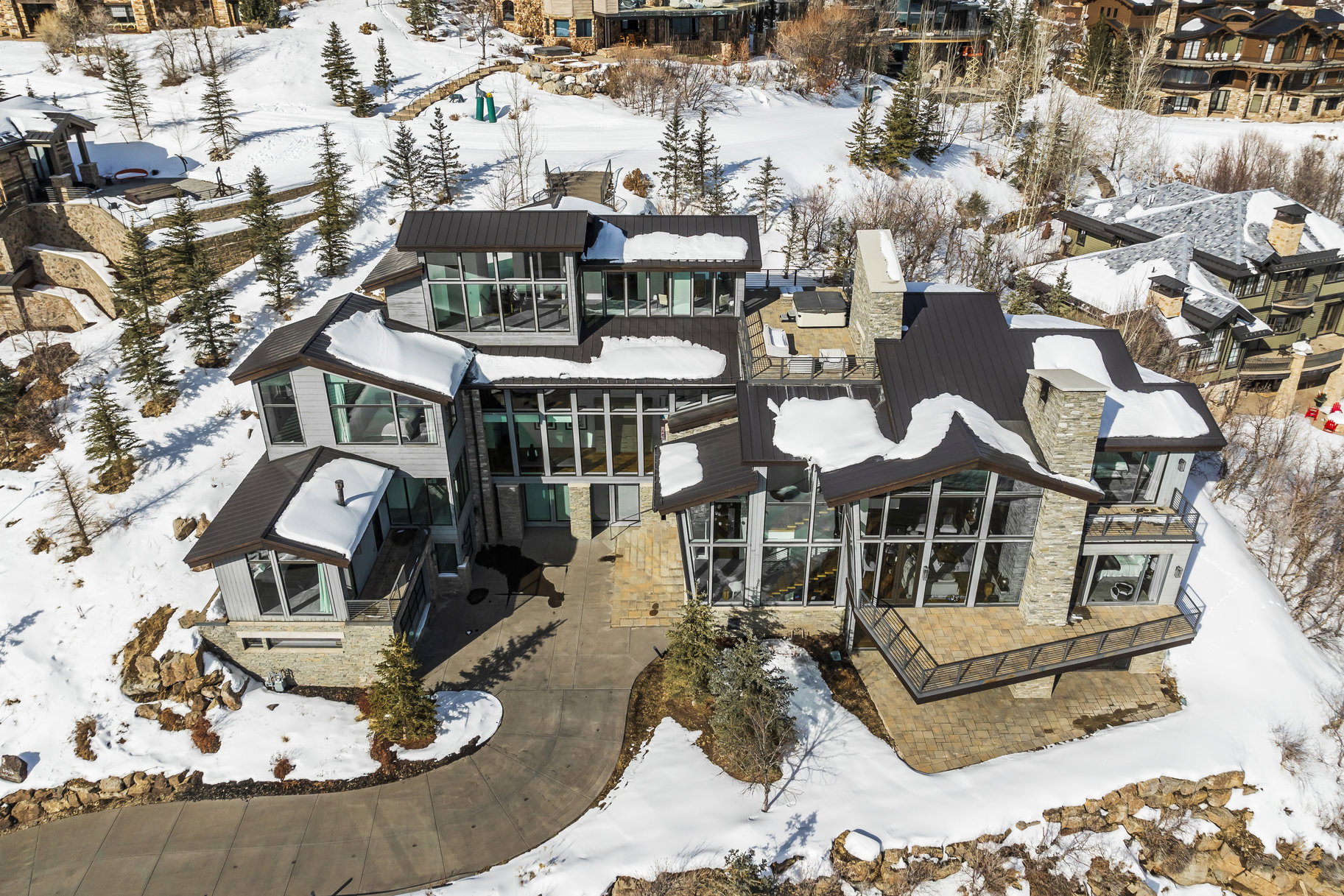 Contemporary multi-level residence featuring extensive floor-to-ceiling windows, a dark metal roof, and stone facade accents
