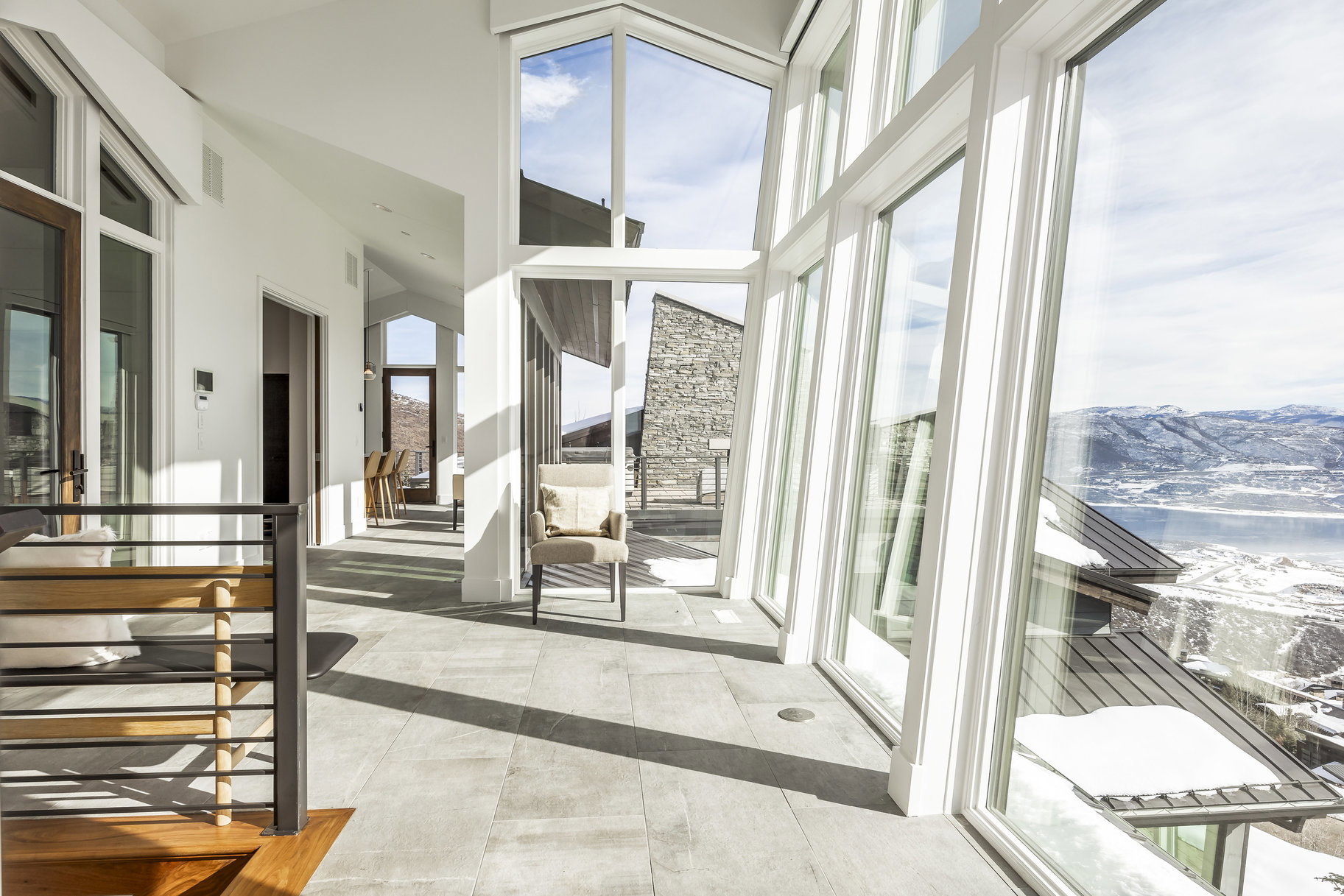 Open-concept interior featuring expansive floor-to-ceiling windows, light-toned tile flooring, and a contemporary wood and metal staircase railing