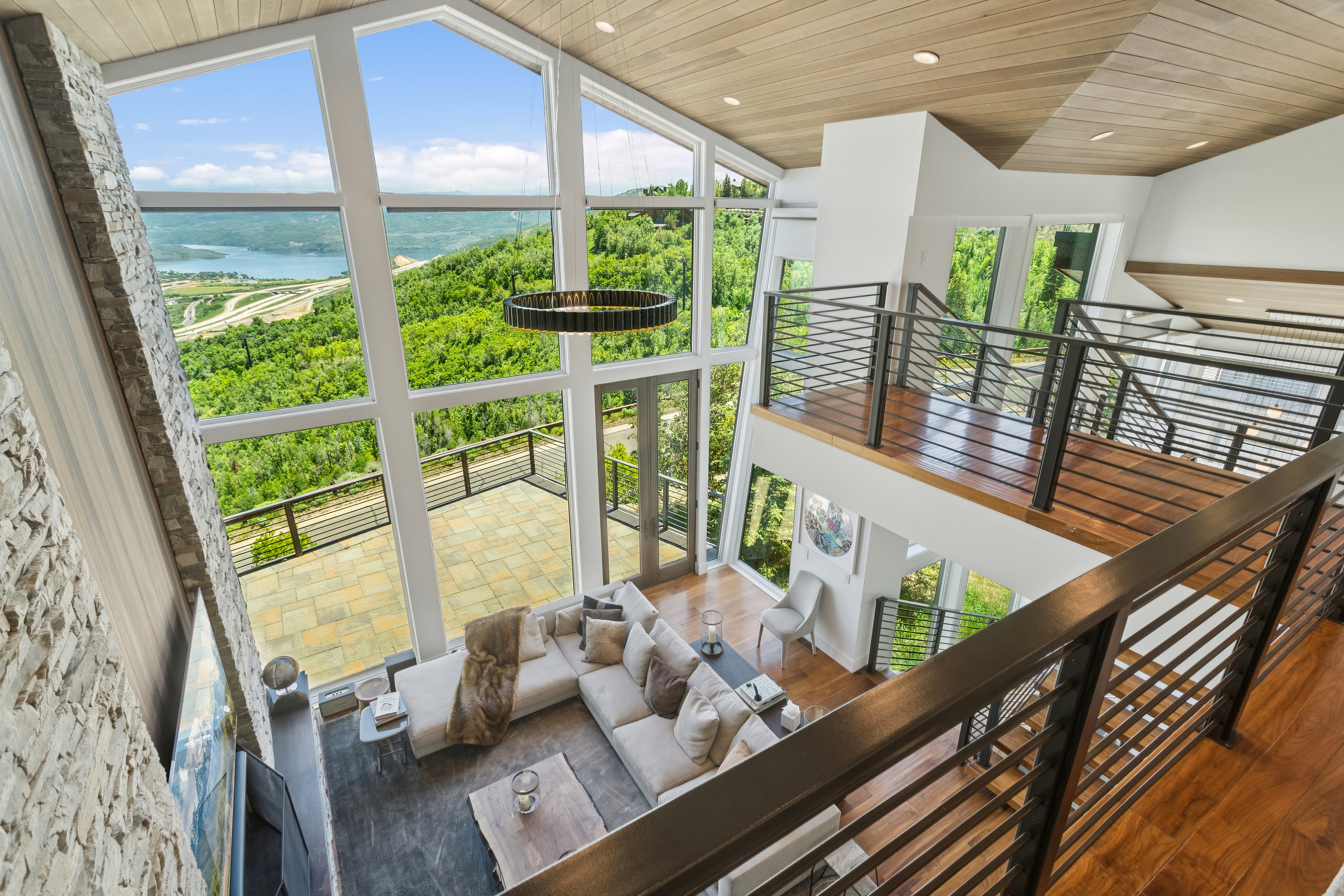 Vaulted great room with expansive window walls, wood-finish ceiling, stone fireplace surround, and multi-level living areas