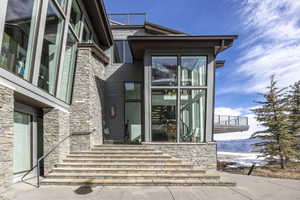 Contemporary exterior featuring stone cladding, multi-pane windows, a prominent glass facade, a large outdoor deck, and a stone staircase