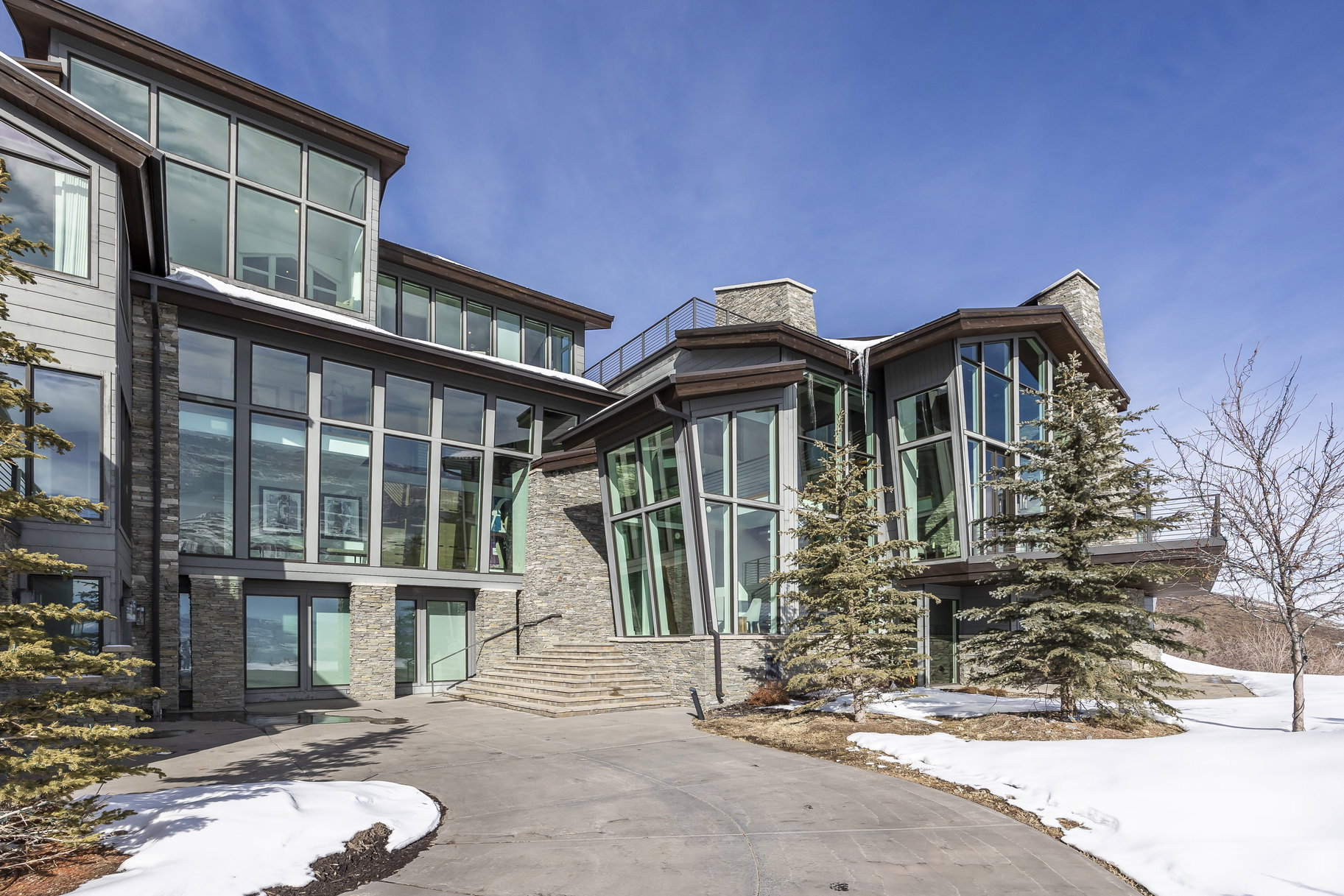 Contemporary architectural design featuring extensive window walls, stone accents, and multiple balconies