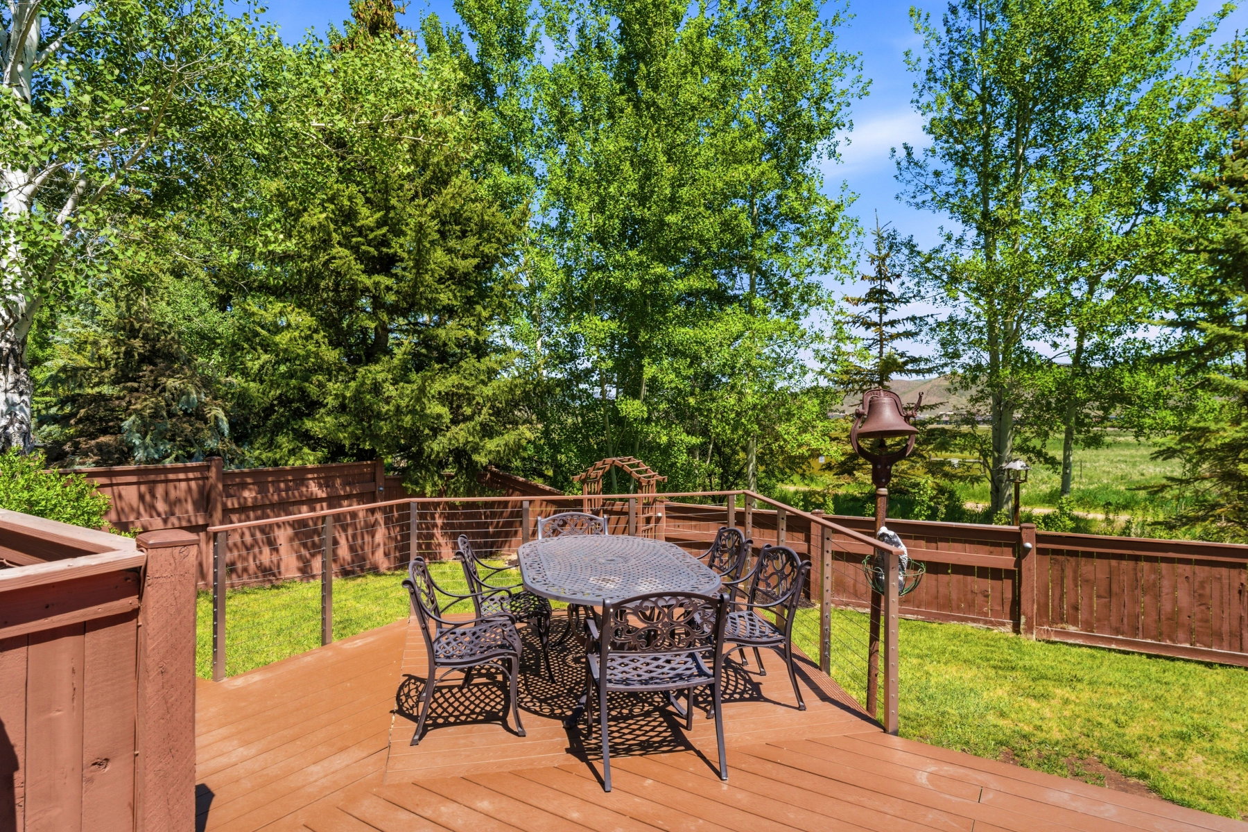 Spacious outdoor deck featuring a rich wood-tone finish, cable railing, and a private fenced yard with established trees and lush lawn