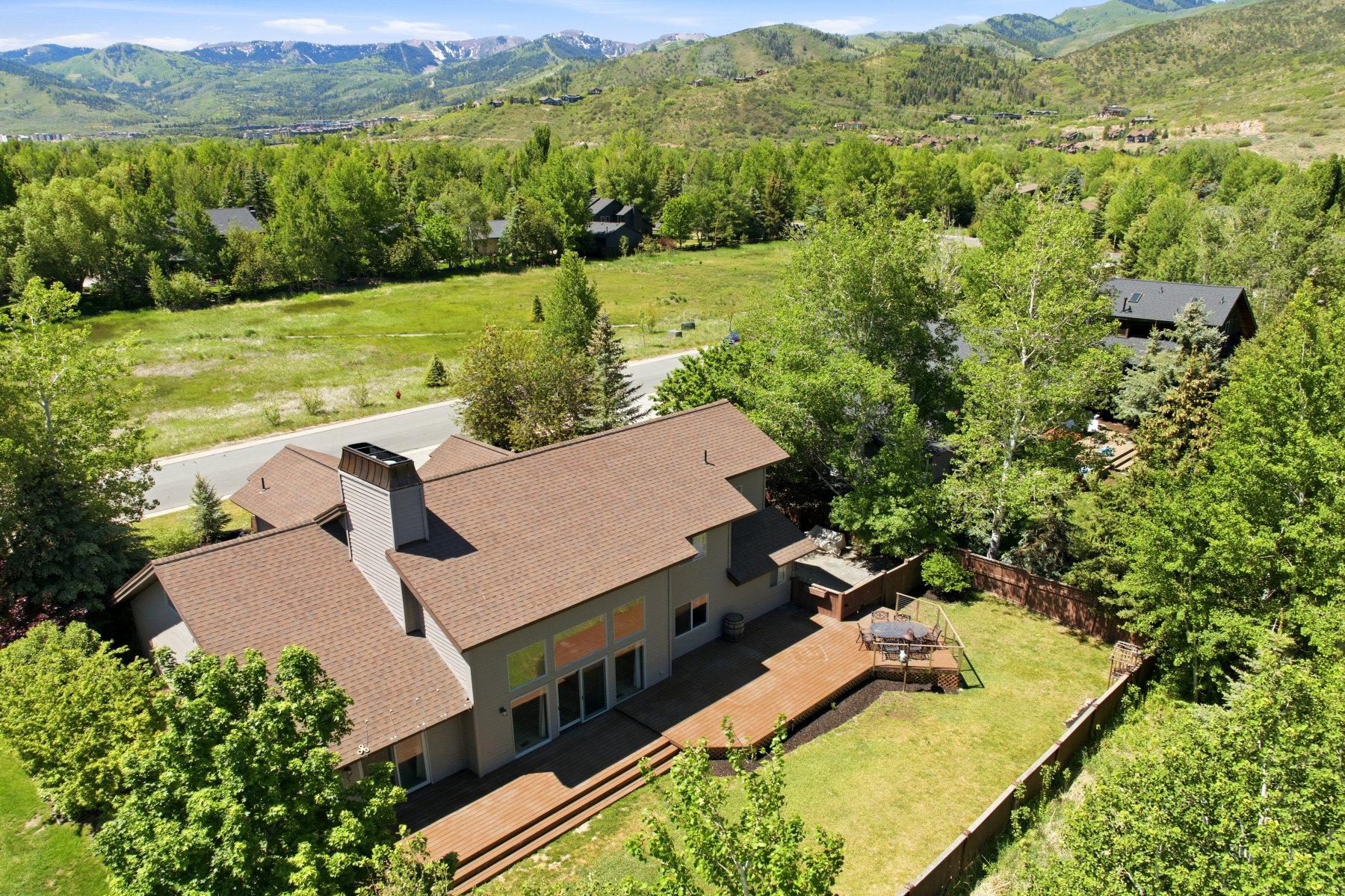 Expansive property featuring a multi-level wood deck, a fenced lawn area, and mature trees providing ample shade