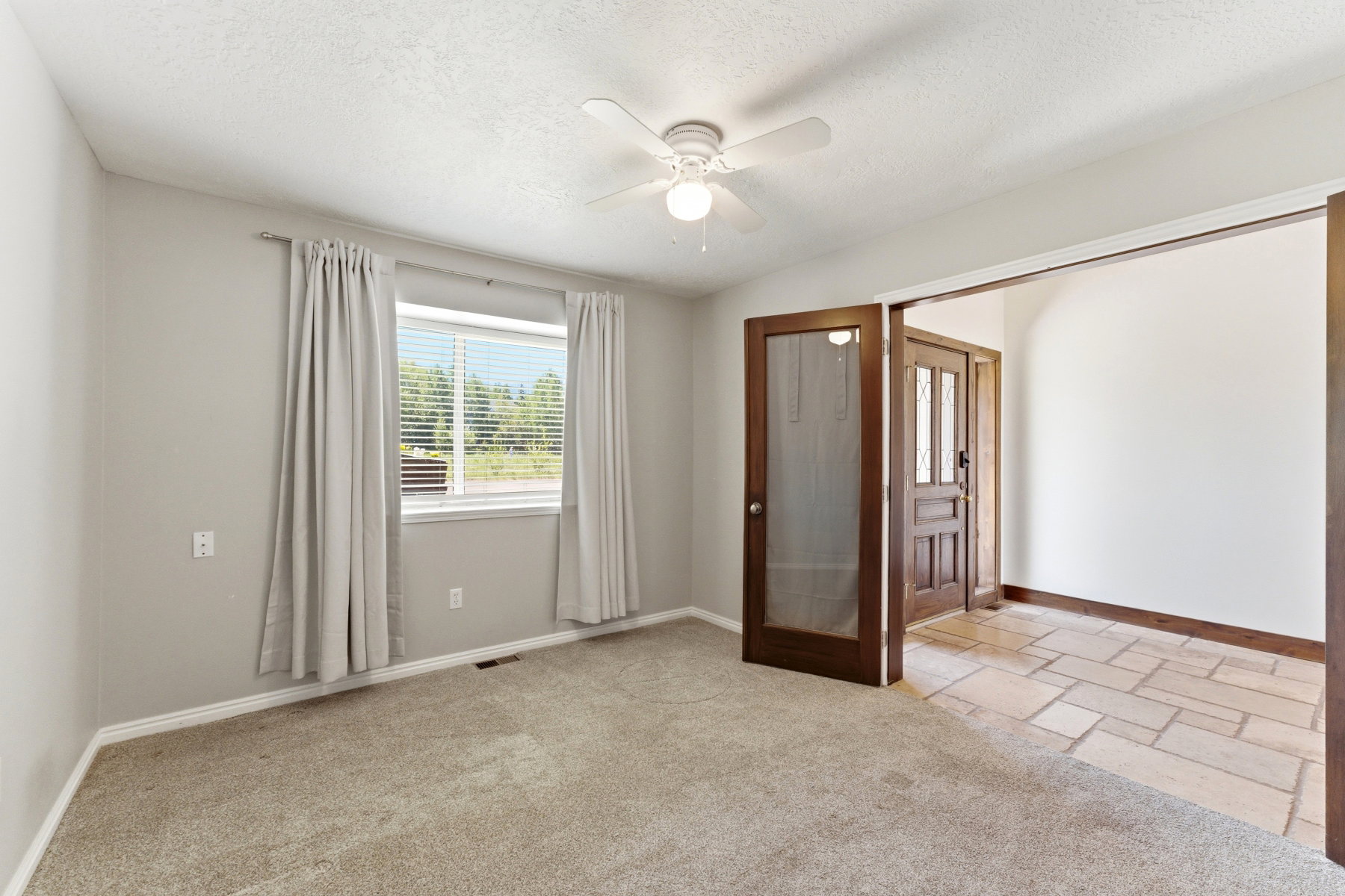 Carpeted room featuring a white ceiling fan, a window with horizontal blinds, and a doorway with a screen door and wood frame