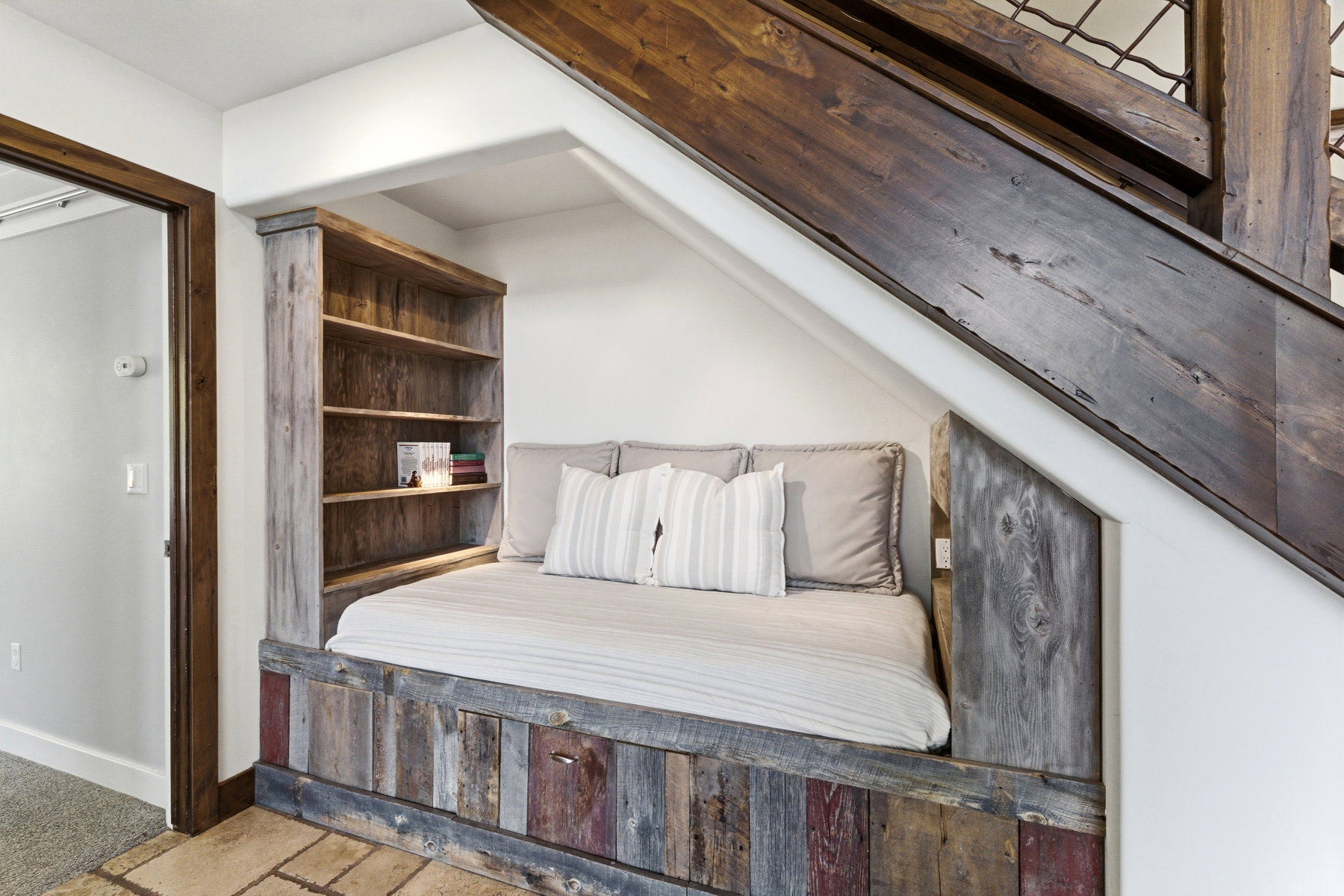Built-in reading nook under a dark wood-finish staircase, featuring a multi-toned wood-finish base and an integrated bookshelf