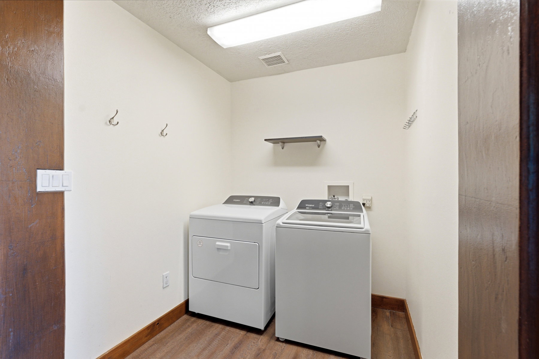 Dedicated laundry space featuring wood-finish flooring, white walls, and a built-in shelf