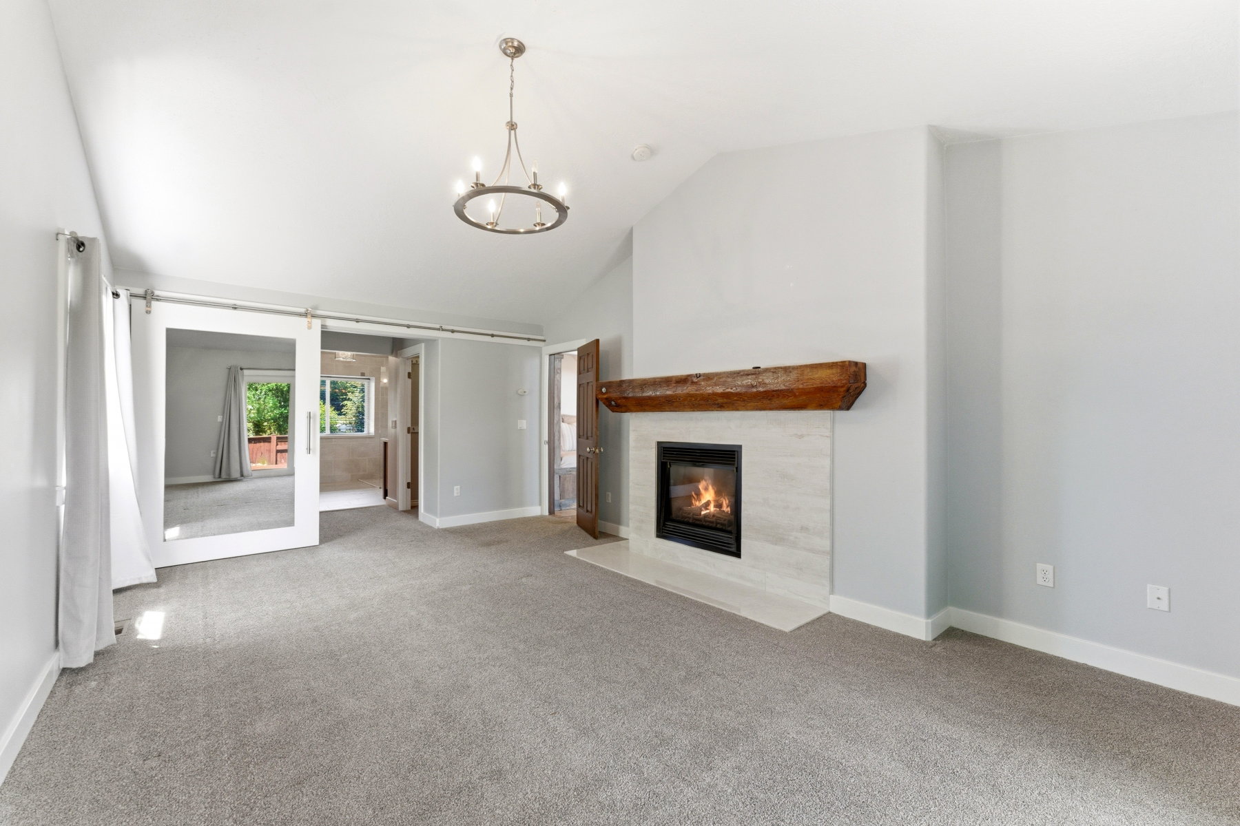Vaulted ceiling with an overhead chandelier, a fireplace featuring a stone surround and wood mantel, light gray wall paint, and gray carpeting