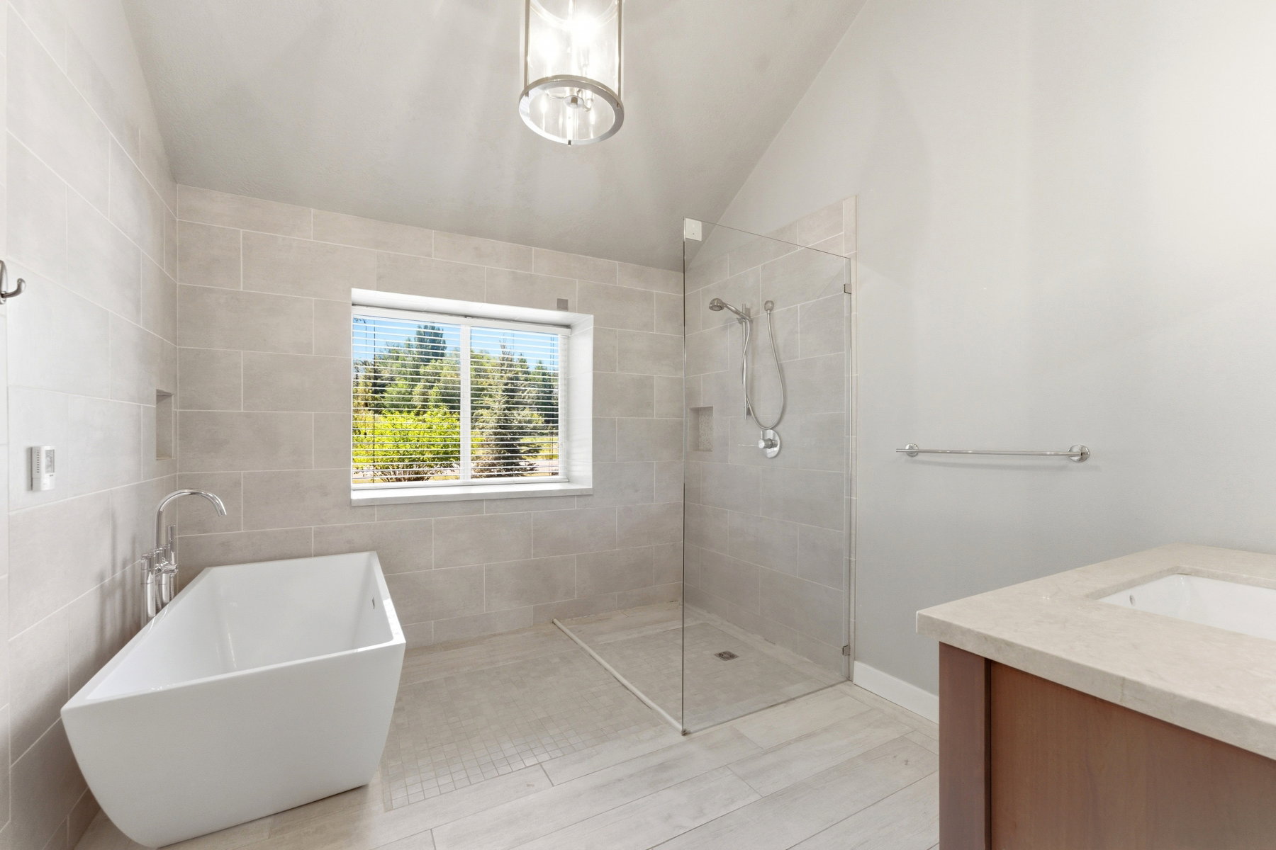 Bathroom featuring a freestanding tub with a floor-mounted faucet, a walk-in shower with a glass enclosure, light-toned tile flooring, and a vanity with an integrated sink and stone countertop