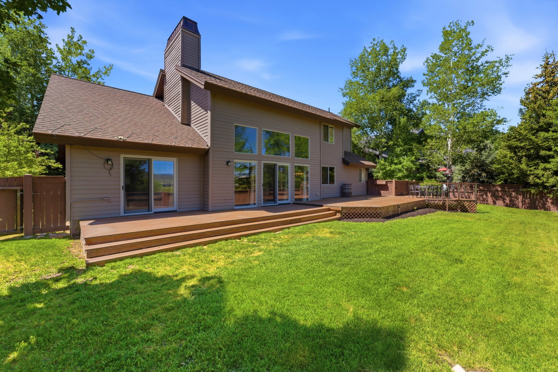 Spacious backyard featuring a multi-level wood deck, expansive green lawn, and mature trees