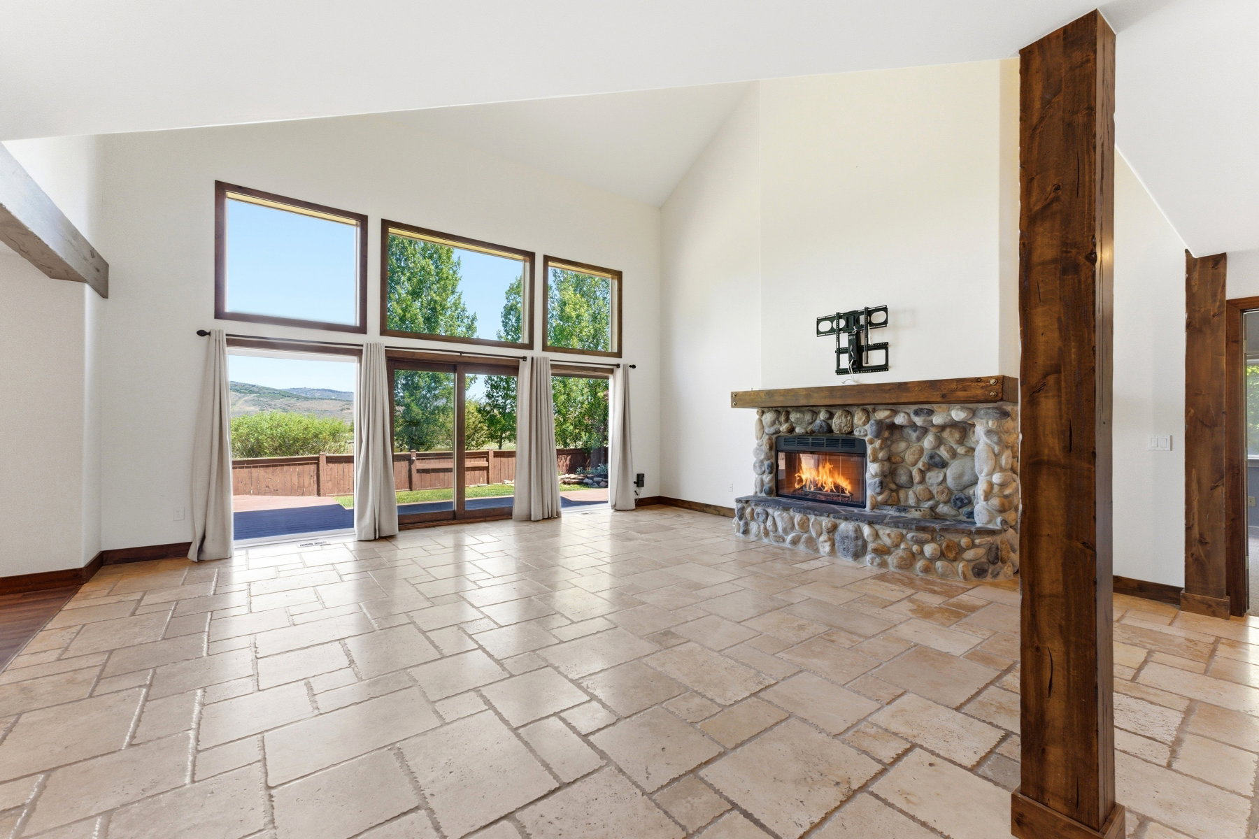 Vaulted ceilings featuring exposed wood beams, a stone fireplace with a wood mantel, and expansive windows with sliding glass doors