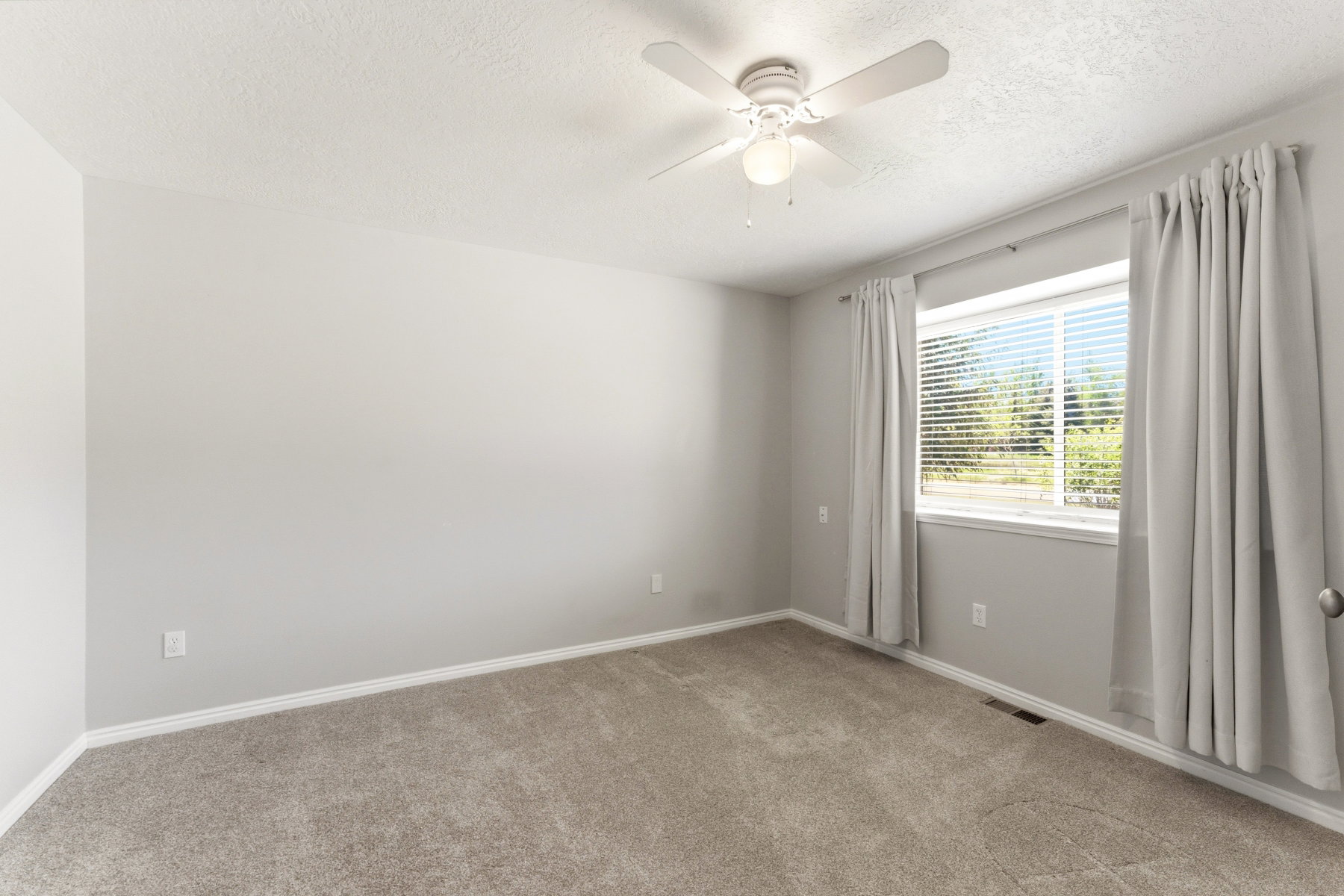 Carpeted room with a ceiling fan light fixture, white trim, and a window with blinds
