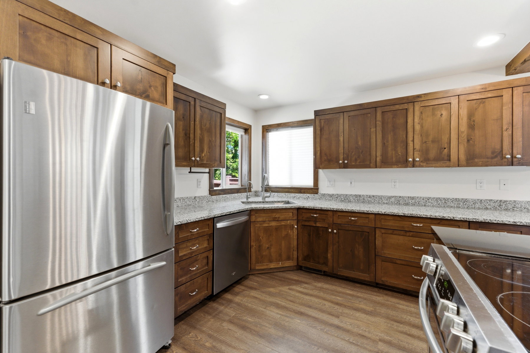 Kitchen featuring stainless steel appliances, wood-finish flooring, granite-style countertops, and rich wood cabinetry